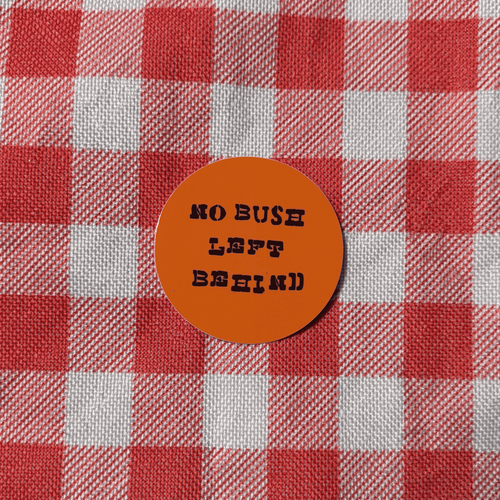 A round orange sticker with black text reading 'NO BUSH LEFT BEHIND' placed on a red and white checkered fabric background.