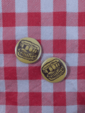 Two round pinback buttons featuring a black cartoon mouth with teeth on a yellow background, placed on a red and white checkered picnic blanket.