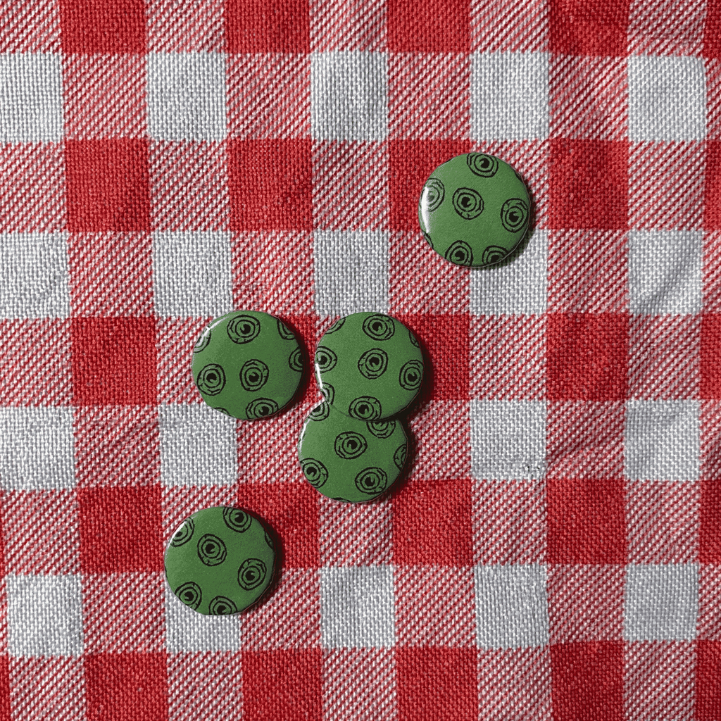 Five green round buttons with a black circular pattern, arranged on a red and white checkered fabric background.