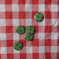 Five green round buttons with a black circular pattern, arranged on a red and white checkered fabric background.